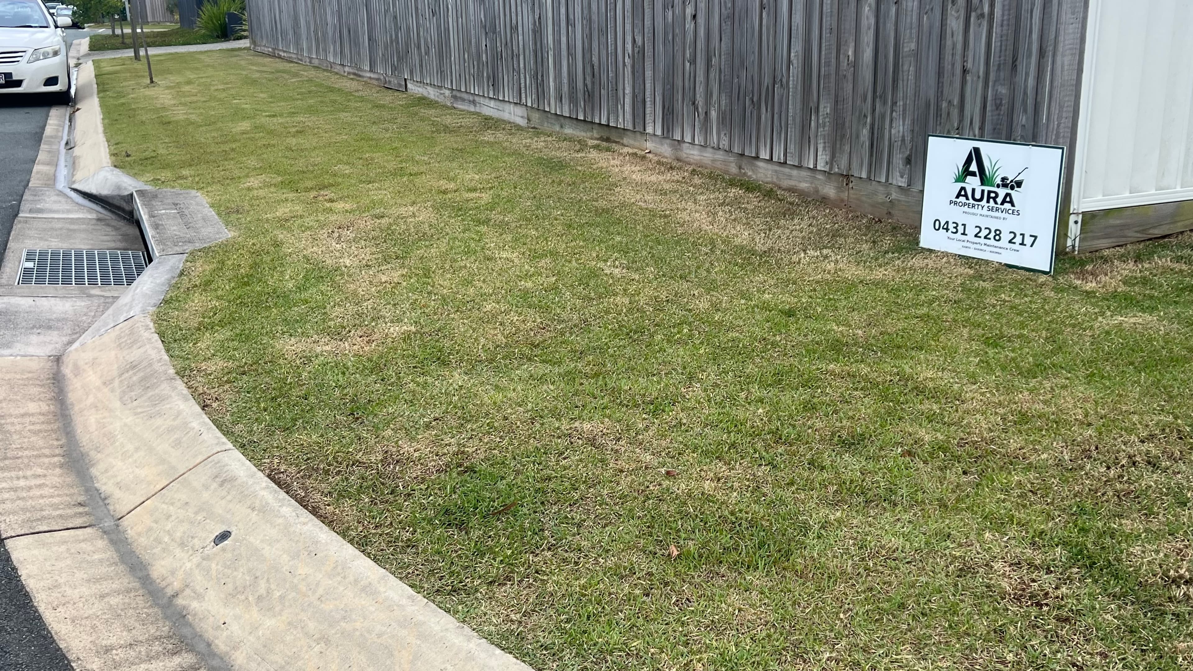 A mowed lawn next to a wooden fence with an Aura Property Services sign.